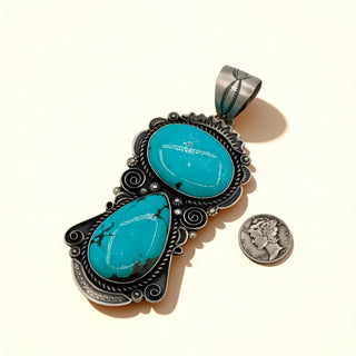 Turquoise stone pendant with intricate silver design on a white background