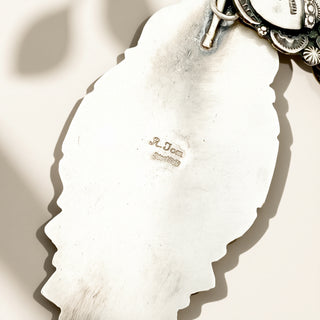 Close-up of a silver jewelry with 'R. Tom' engraving on a neutral background