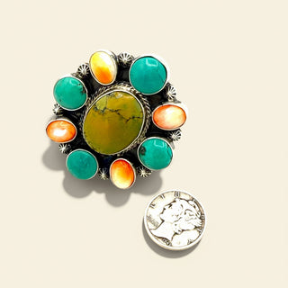 Multicolored stone ring with a coin for size comparison on a beige background