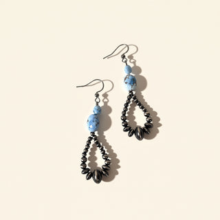 Pair of beaded earrings with blue and black beads on a beige background