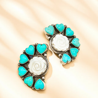 Pair of earrings with turquoise heart-shaped stones and a central white stone on a beige background