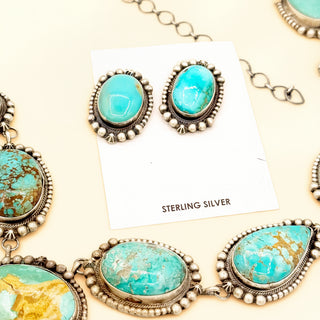 Turquoise stone earrings with silver accents on a beige background