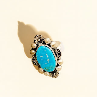 Ring with turquoise stone and gold accents on a beige background