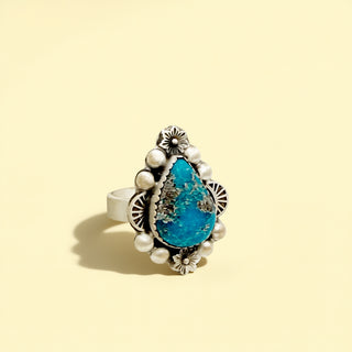 Ring with turquoise stone and pearl accents on a beige background