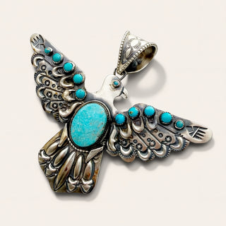 A sterling silver bird pendant featuring turquoise inlay, photographed on a light beige background.