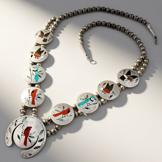 A silver-toned beaded necklace with oval inlay discs featuring colorful bird and floral motifs, photographed on a light gray background with soft shadows.