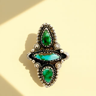 Silver ring with green stones on a beige background