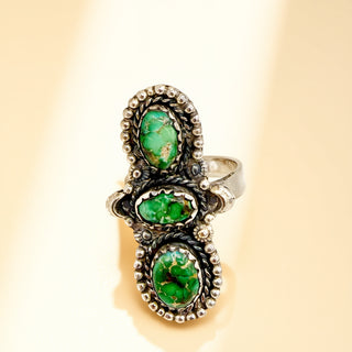 Silver ring with green stones on a beige background