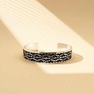 Silver cuff with designs on a beige background