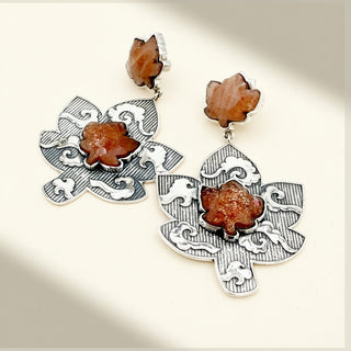 Ornate silver earrings with brown stone accents on a light background