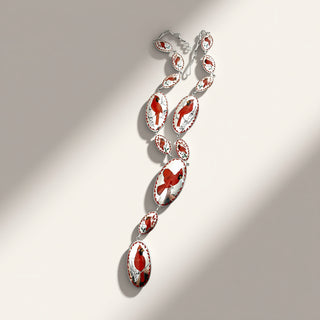 A silver-toned statement necklace with multiple elongated oval links, each featuring a red and white abstract pattern, displayed on a warm beige background with soft diagonal shadows.