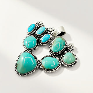 A sterling silver multi-stone pendant featuring seven turquoise-colored cabochon gemstones in a traditional Southwestern style, set against a clean white background.