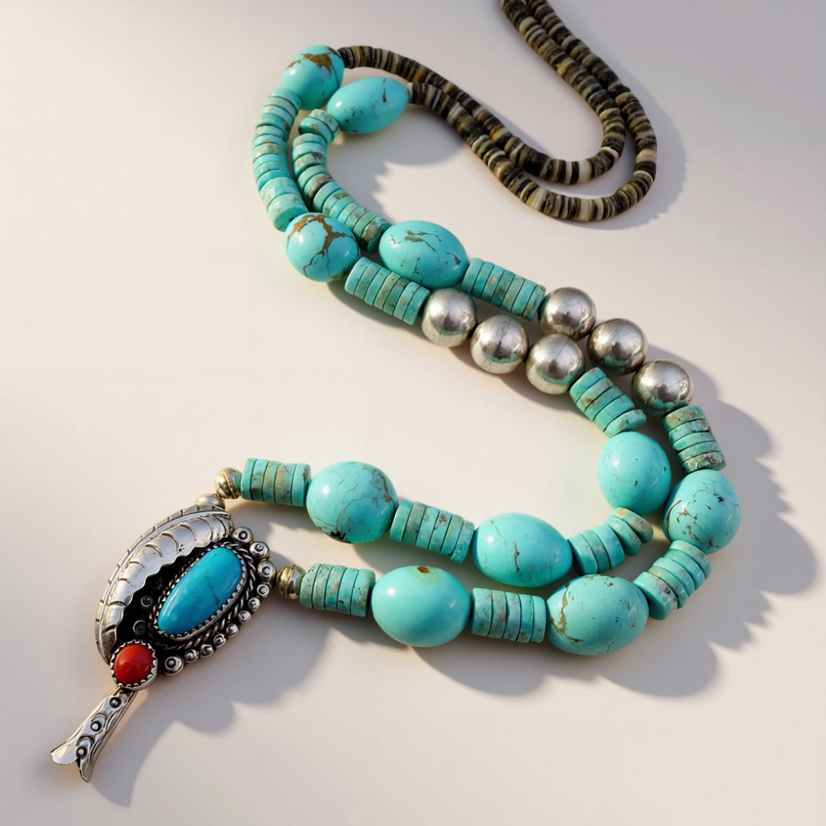 Turquoise beaded necklace with silver and red accents on a light background