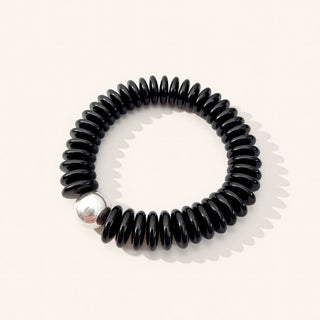 Black coil bracelet with a silver bead on a white background