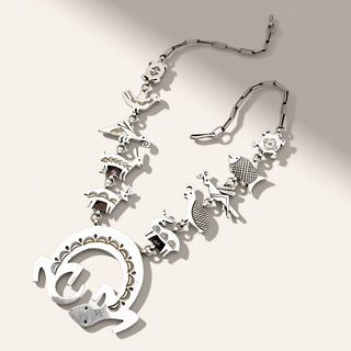 A silver-toned metal necklace featuring a large circular pendant connected to a chain of small animal and floral charms, displayed on a light beige background.
