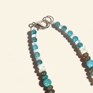 Beaded necklace with turquoise and white beads on a beige background
