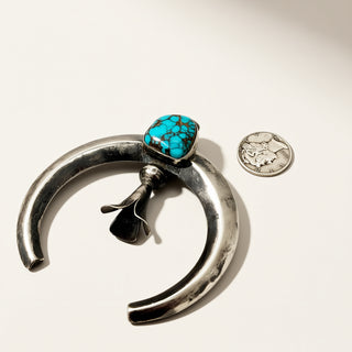 Silver pendant with turquoise stone next to a coin on a white background