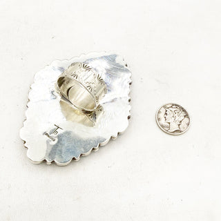 Silver ring on a silver dish with a quarter for scale on a white background