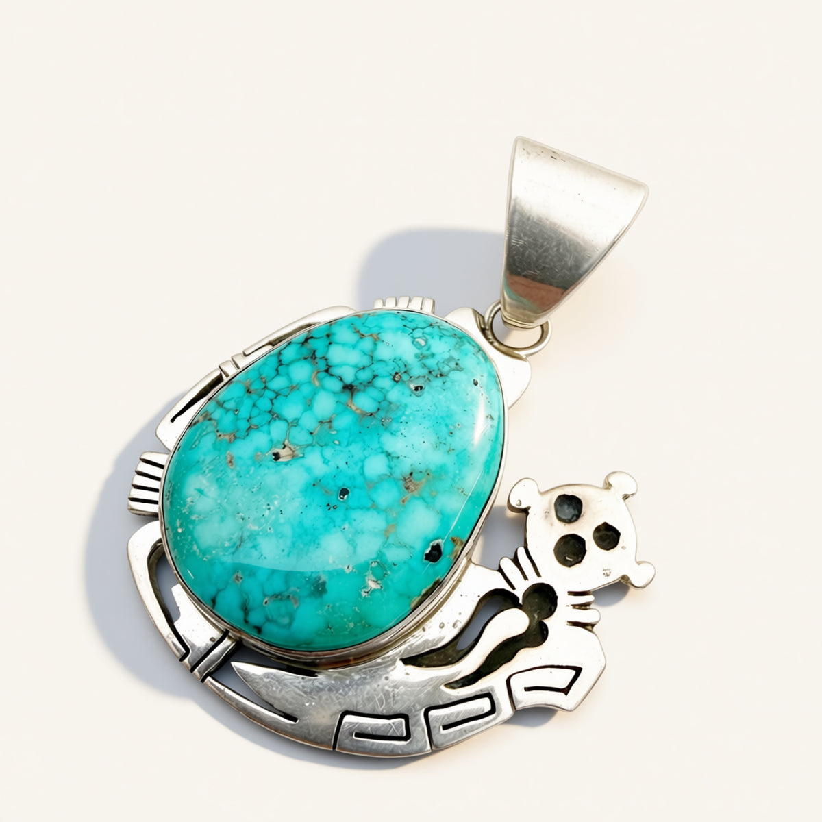 A sterling silver pendant featuring a large oval turquoise stone with natural matrix patterns and a small silver animal motif, photographed on a light cream background.