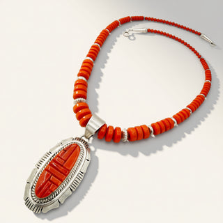 A Southwestern-style necklace featuring a large oval carved red agate pendant set in silver, surrounded by a beaded strand on a light gray background.
