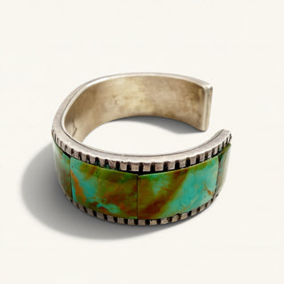 silver cuff with green stones on a beige background
