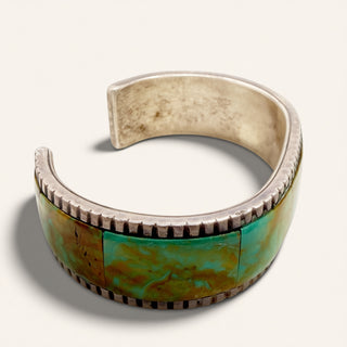 silver cuff with a green stone on a beige background