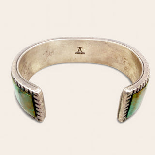 silver cuff with "A" engraving and green stones on a beige backgorund