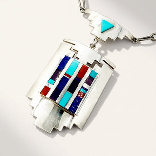 A silver geometric pendant necklace featuring a Southwestern-style inlay design with turquoise, lapis lazuli, red, and black striped accents, shown on a clean white background.