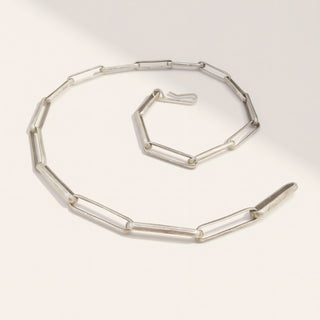 a silver paperclip chain necklace on a beige background