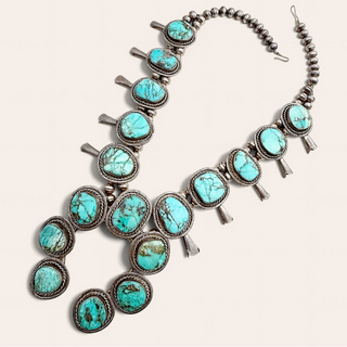 A Southwestern-style silver necklace featuring multiple oval turquoise stones in textured silver bezels, arranged in a cascading pattern on a light beige background.