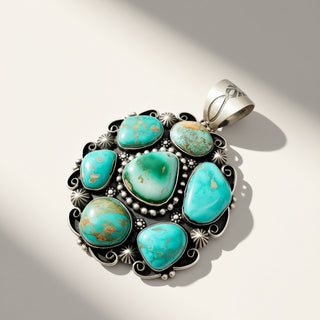 A silver pendant featuring seven turquoise-colored stones with brown matrix, set in an ornate filigree design with small silver beads and star details, photographed on a light beige background with soft shadows.