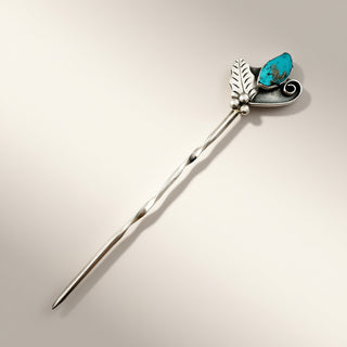 A sterling silver hair stick featuring a twisted stem, a leaf and heart design, and a turquoise stone accent, shown on a neutral beige background.