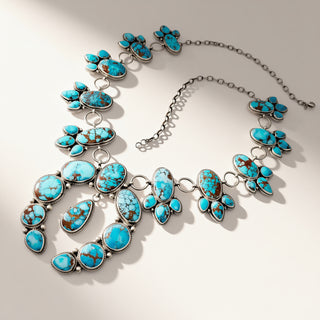 A silver-toned statement necklace featuring multiple turquoise-colored stones with brown matrix, arranged in floral and geometric patterns on a light beige background.