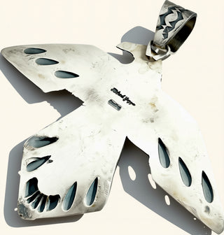 The back of a silver bird pendant showing the name Richard Yazza on a cream background