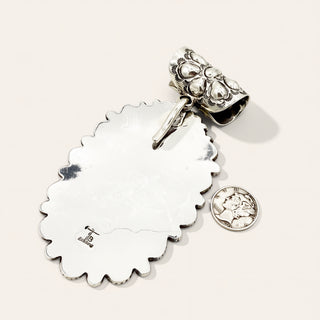Silver charm with a round coin and scalloped edge on a white background