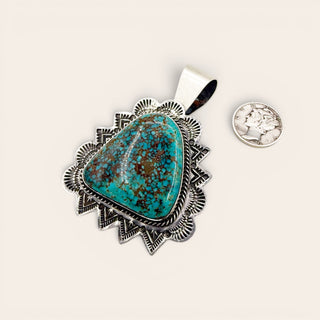 Turquoise pendant with silver setting next to a quarter for scale on a white background