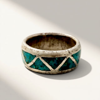 A wide silver ring featuring a textured turquoise green inlay pattern, photographed on a light gray background with soft diagonal shadows.