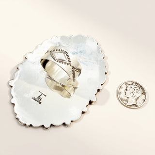 Silver ring with tribal design on a shell next to a coin for scale