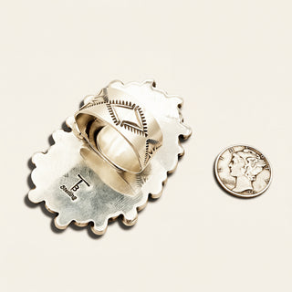 Gold ring with intricate design on a beige background, next to a U.S. quarter coin for scale.