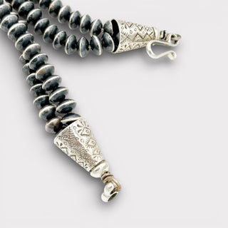 Necklace with black beads and silver clasp on a light gray background