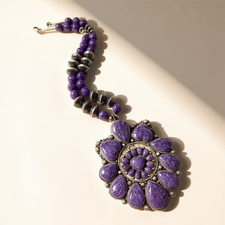 Purple beaded necklace with a decorative pendant on a light background