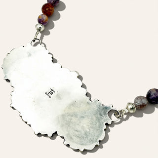 Silver pendant with purple beads on a beige background
