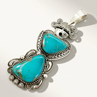 silver maiden pendant with two turquoise stones on a beige background