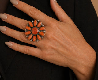 Close-up of a hand wearing a sunflower-shaped ring with orange stones on a black background