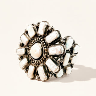 A wide silver-toned cuff cuff decorated with multiple white mother-of-pearl cabochon stones, photographed on a clean off-white background with a soft shadow.